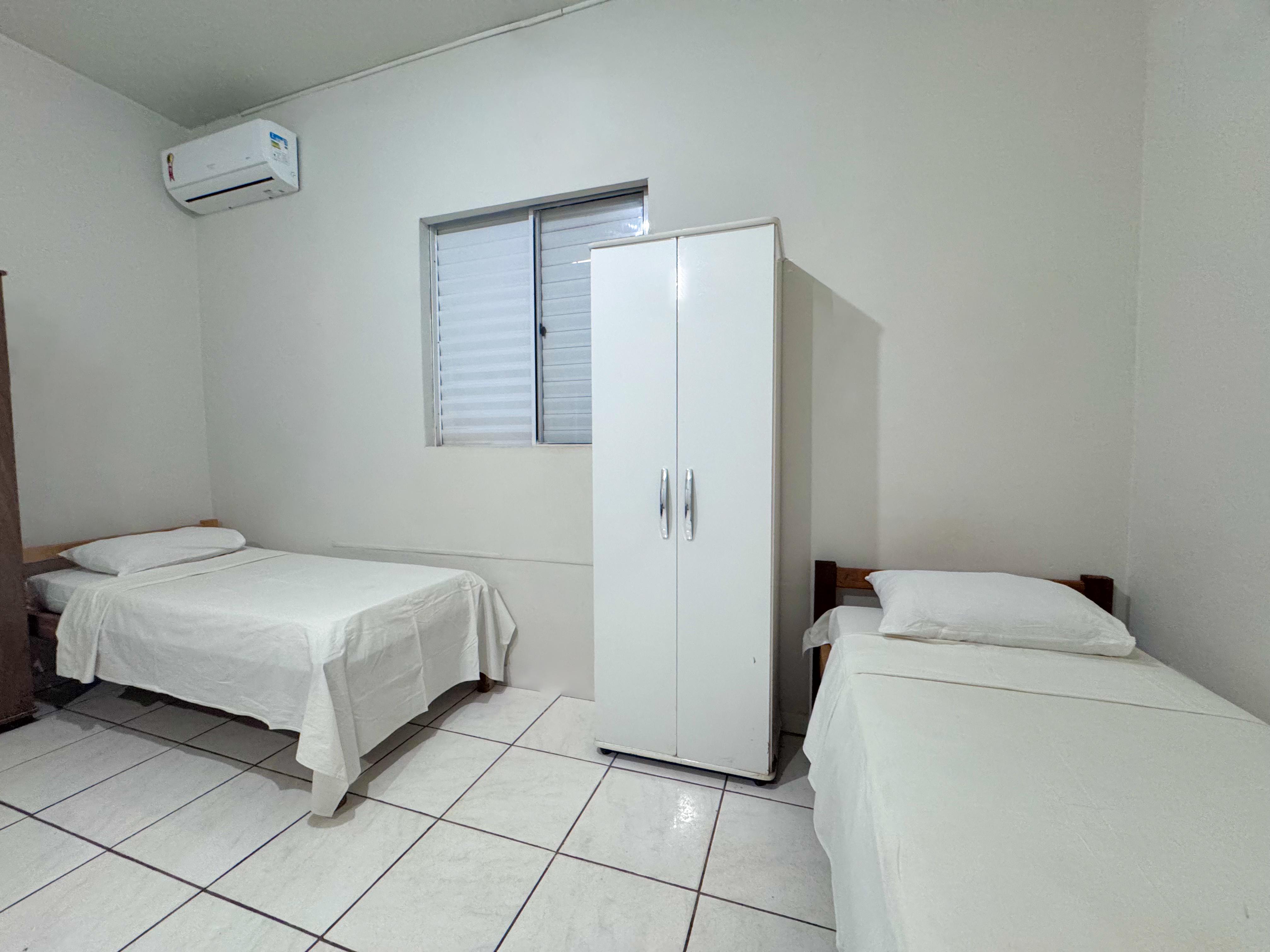 Quarto com duas camas de solteiro, guarda-roupa e ar-condicionado