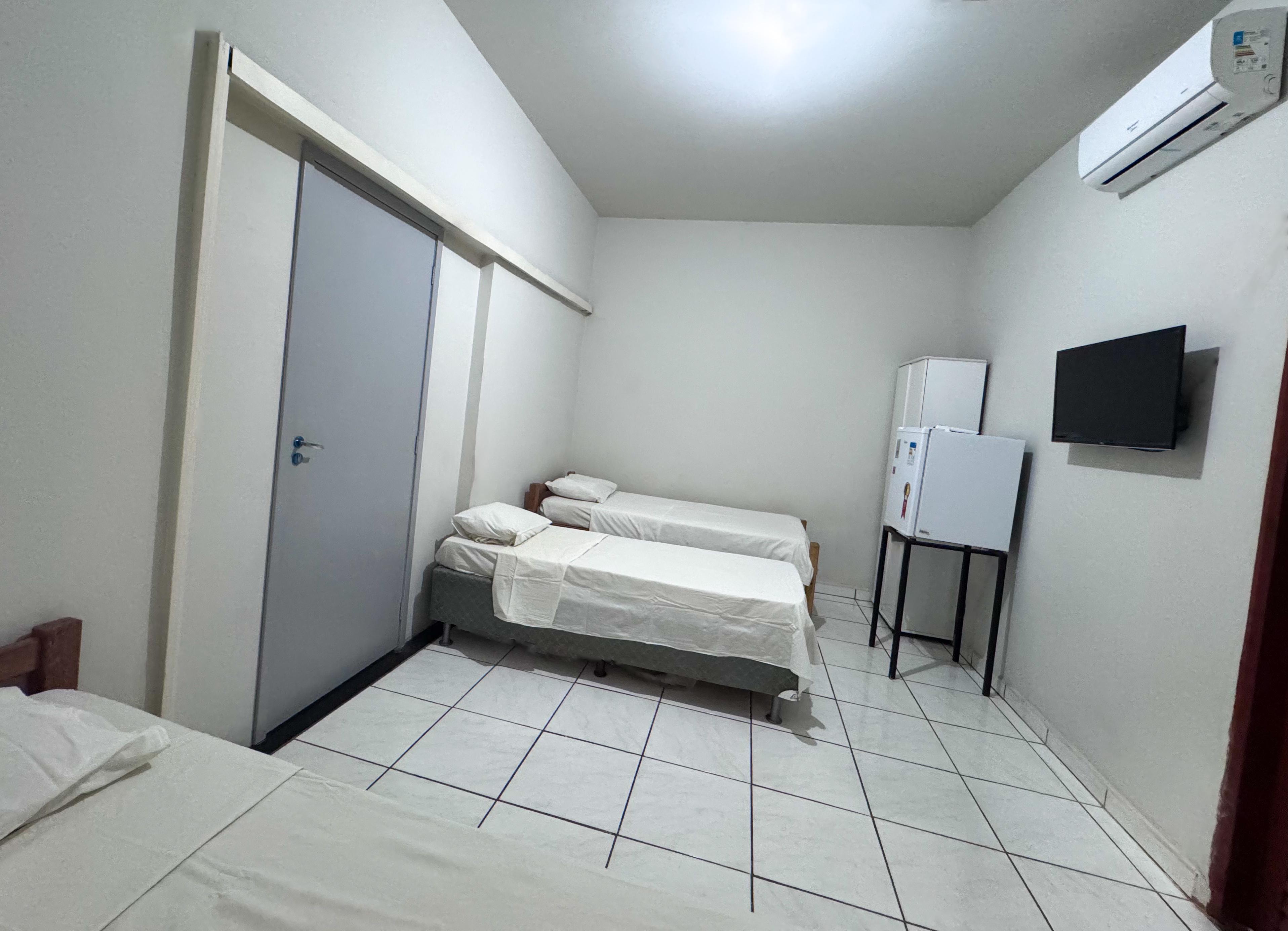Quarto com camas de solteiro, TV de parede, ar-condicionado e frigobar